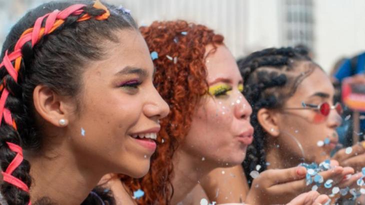 Foto van drie vrouwen die confetti wegblazen om internationale vrouwendag te vieren.