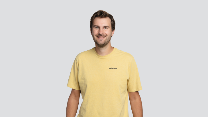 Lucas Nutbey, DEPT®'s director of strategy, lachend, in geel tshirt en grijze achtergrond